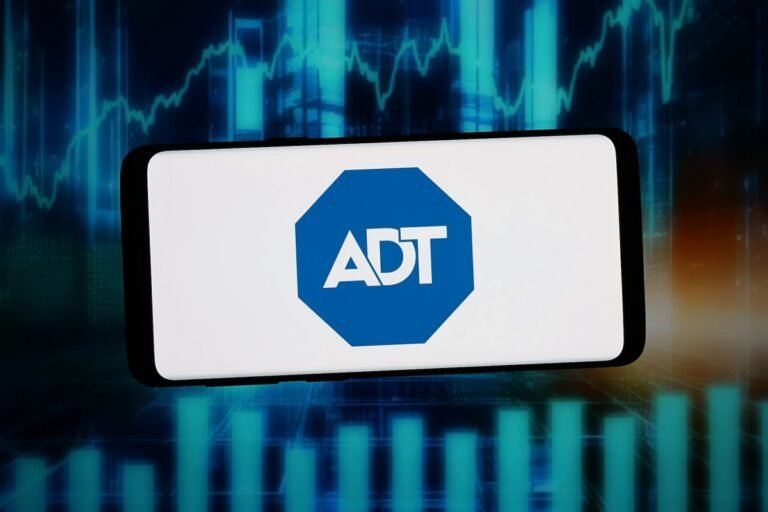 Smartphone displaying ADT logo with a digital stock market chart in the background.