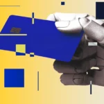 Robotic hand holding a blue credit card against a yellow background with scattered geometric shapes.