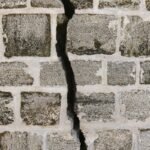 Close-up of a cracked stone wall with gray bricks and visible mortar lines