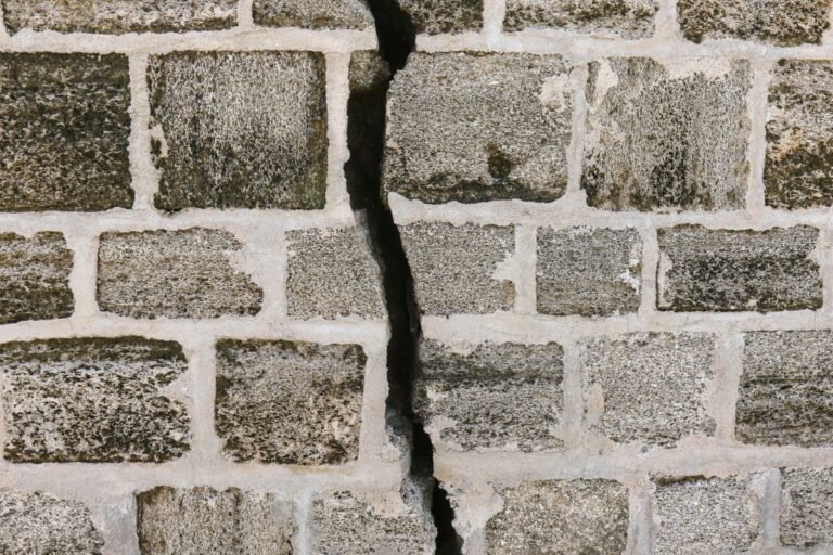 Close-up of a cracked stone wall with gray bricks and visible mortar lines