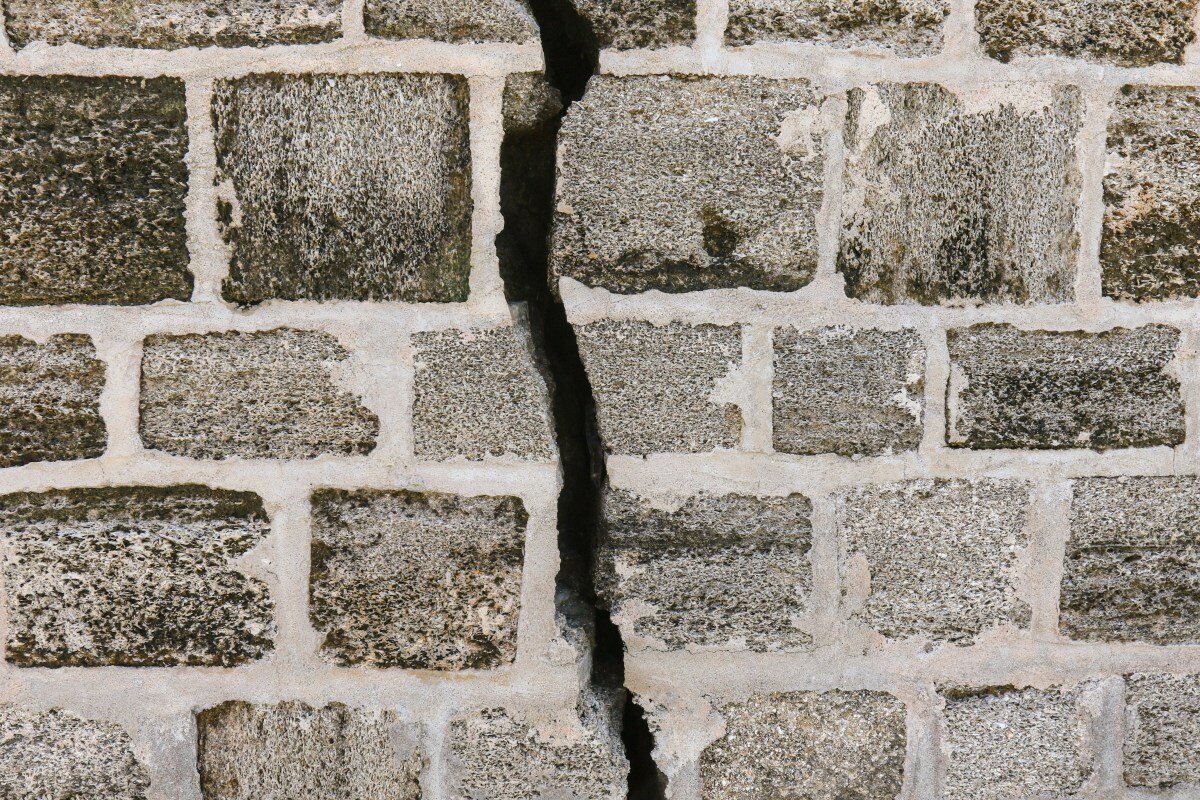 Close-up of a cracked stone wall with gray bricks and visible mortar lines
