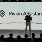 Speaker on stage presents Rivian Assistant, with logo and colorful wave line on screen, audience in foreground.