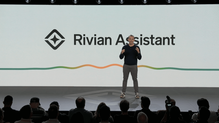 Speaker on stage presents Rivian Assistant, with logo and colorful wave line on screen, audience in foreground.