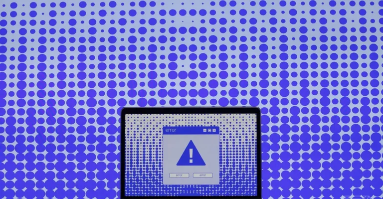 Laptop screen showing a large error alert icon, set against a background of blue dots on a gradient backdrop.