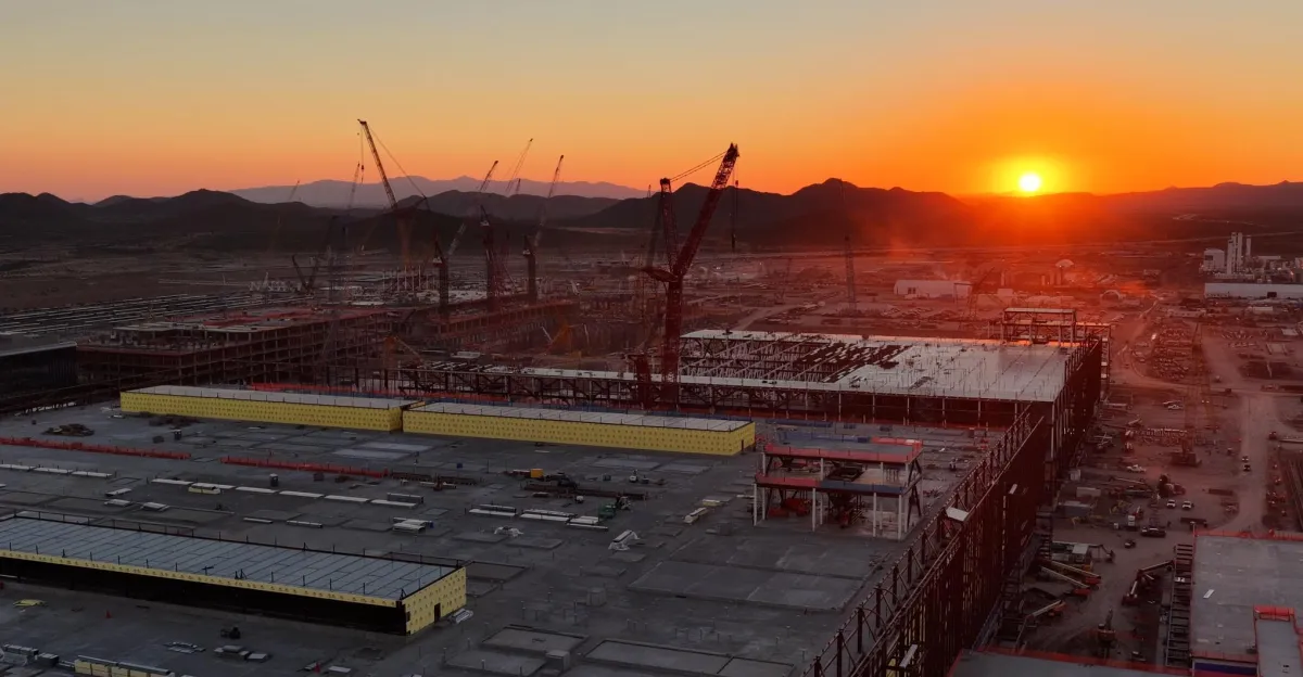 Aerial view of a construction site at sunset with cranes, large buildings, and distant mountains.