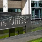 Home Office sign outside a modern building with glass doors and two security personnel in the background.