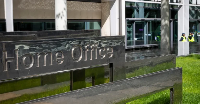 Home Office sign outside a modern building with glass doors and two security personnel in the background.