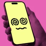 Hand holding a smartphone with a yellow screen displaying a pixelated face with spiral eyes, pink background.