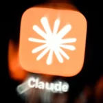 Blurry logo of Claude app featuring a white starburst on an orange background with "Claude" text below.