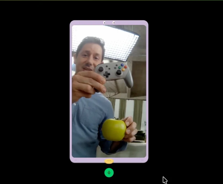 Man on a video call shows a game controller and a green apple, with a microphone icon at the bottom of the screen.