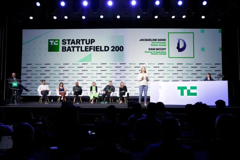 Panelists seated on stage at TechCrunch Startup Battlefield 200, presenter speaking, large screen displays event details.