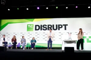 Panelists seated on stage with a speaker standing, TechCrunch Disrupt logo displayed in the background.
