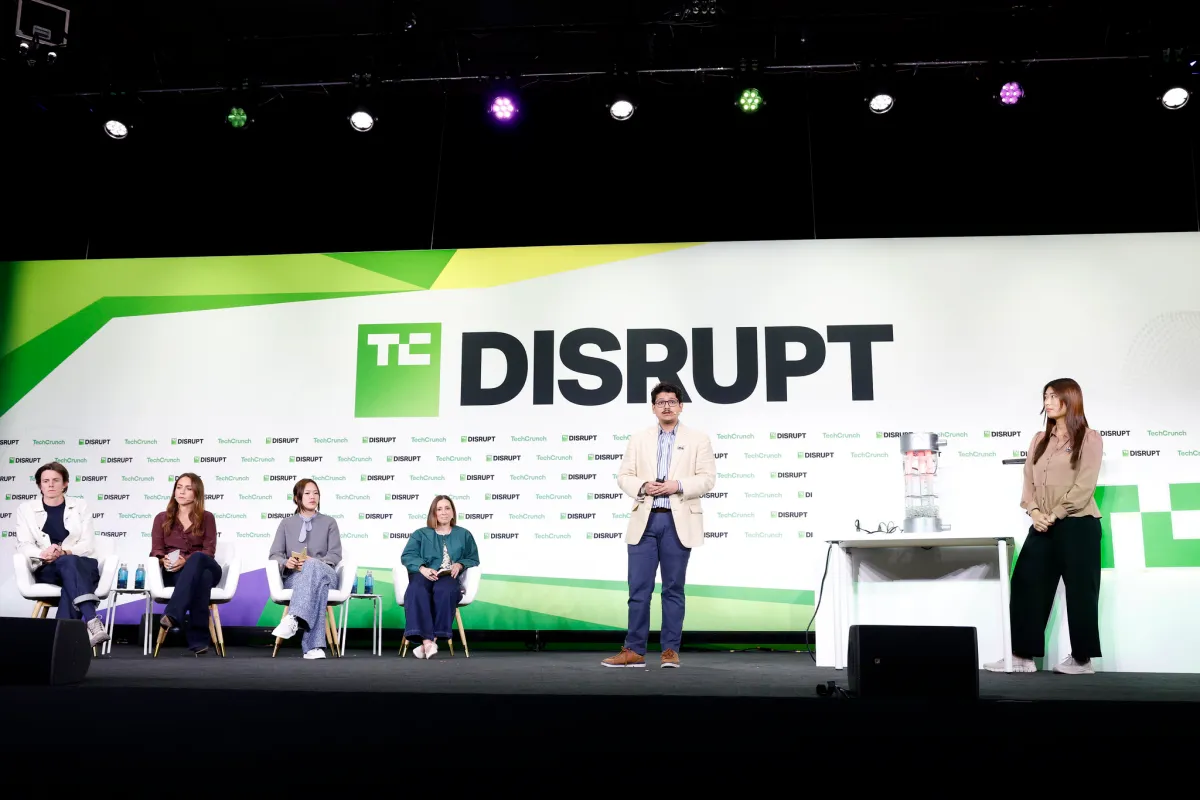 Panelists seated on stage with a speaker standing, TechCrunch Disrupt logo displayed in the background.