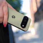 Person holding a gold smartphone with a "G" logo outdoors, showing rear cameras and wearing rings.
