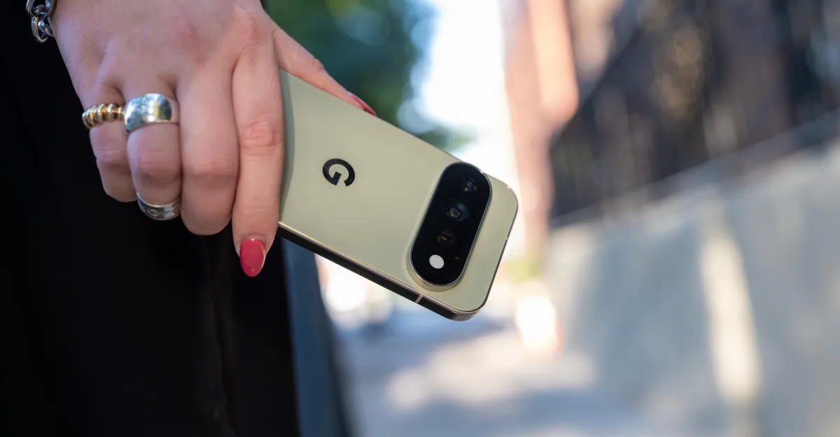 Person holding a gold smartphone with a "G" logo outdoors, showing rear cameras and wearing rings.