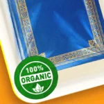 Blue book with gold decorative border on a white tray, green "100% Organic" seal in the corner, orange background.