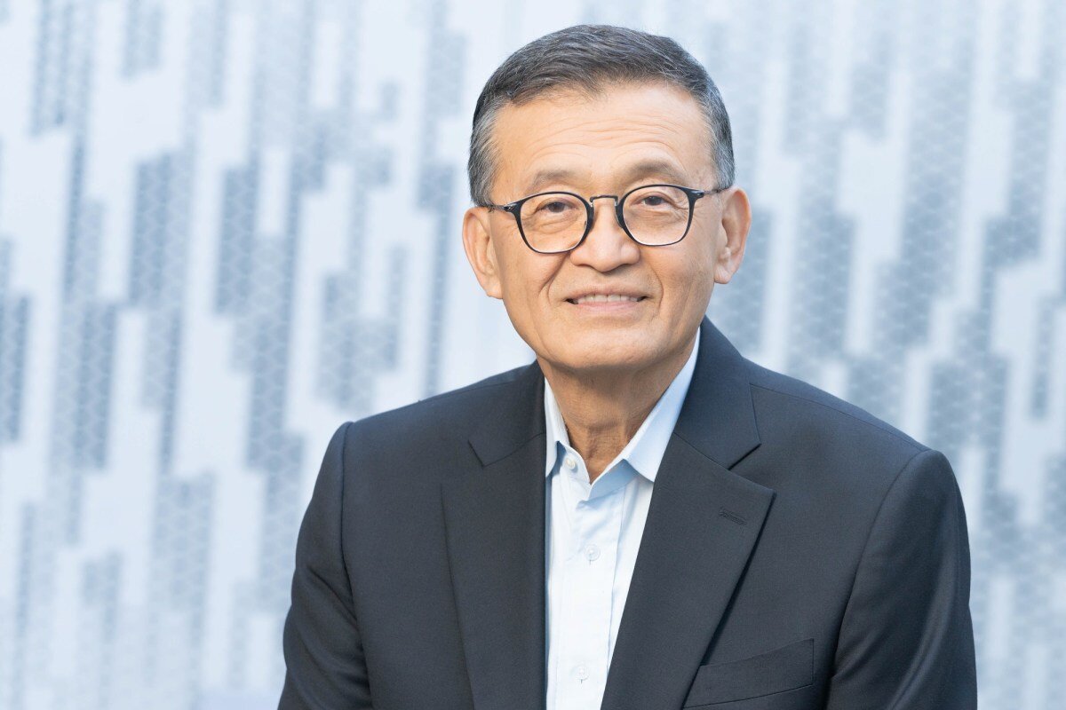 Smiling man in glasses and suit jacket against a patterned background.