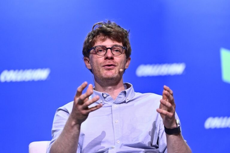 Man with glasses and a microphone speaks on stage against a blue background with "Collision" text.