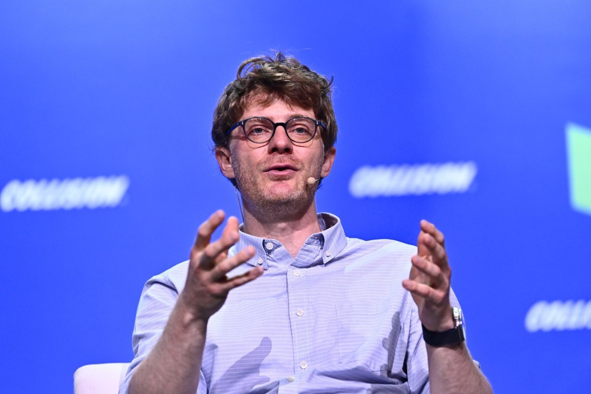 Man with glasses and a microphone speaks on stage against a blue background with "Collision" text.