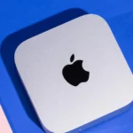 Silver Apple Mac Mini on a blue and pink background, featuring a black Apple logo on top.