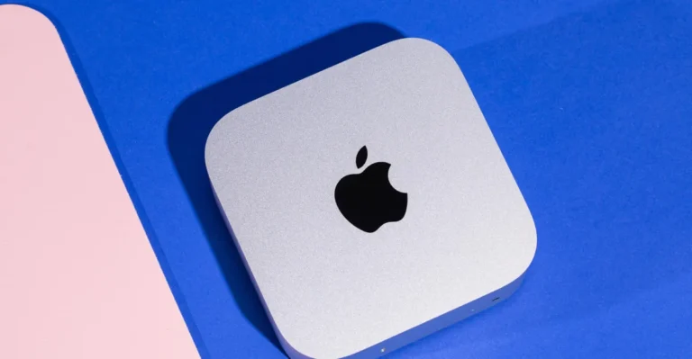 Silver Apple Mac Mini on a blue and pink background, featuring a black Apple logo on top.
