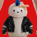 Cartoon figure with blue mohawk and bandage wears a studded jacket, standing between high-heeled legs against a red backgr...