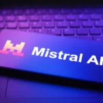 Smartphone displaying Mistral AI logo on a laptop keyboard, illuminated by purple and blue light.