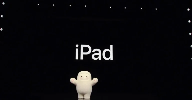 Cute white figure stands on stage with "iPad" displayed on a large screen above, surrounded by small lights