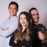 Three people standing with arms crossed, smiling against a plain background.