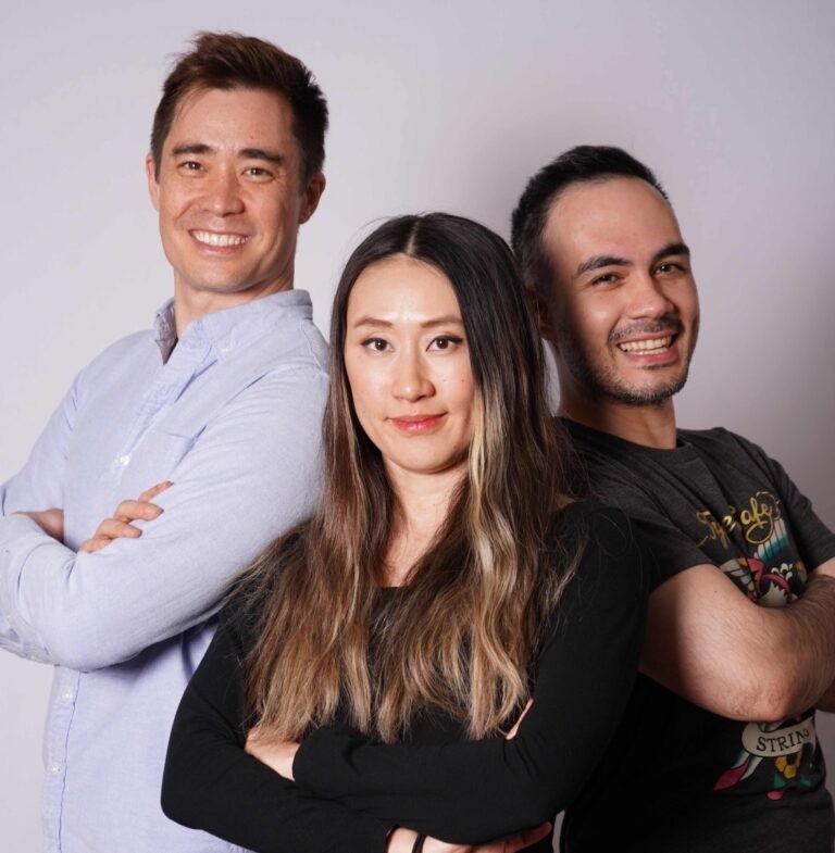 Three people standing with arms crossed, smiling against a plain background.