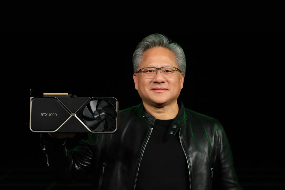 Person in a black jacket holds an Nvidia RTX 4090 graphics card against a dark background.