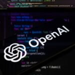 OpenAI logo on a smartphone screen with blurred computer code in the background.