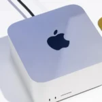 Apple Mac Studio on a white surface with a partial view of a laptop on a yellow mat.