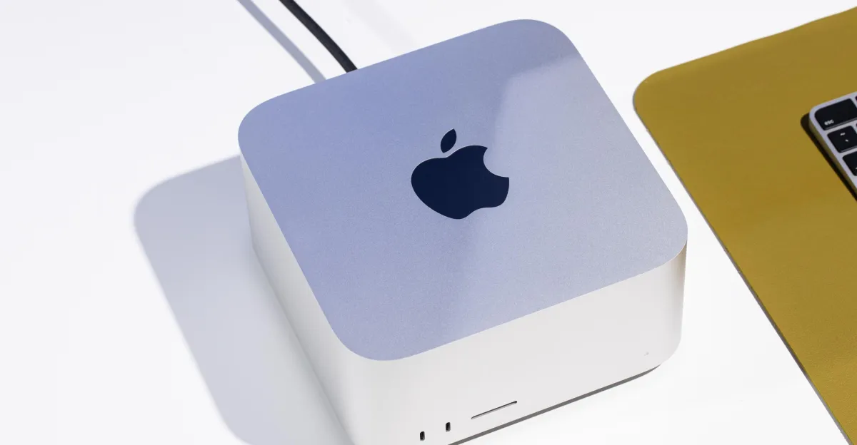 Apple Mac Studio on a white surface with a partial view of a laptop on a yellow mat.