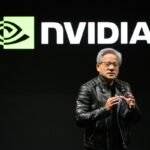 Person in a black leather jacket speaking on stage, Nvidia logo displayed on screen behind them.