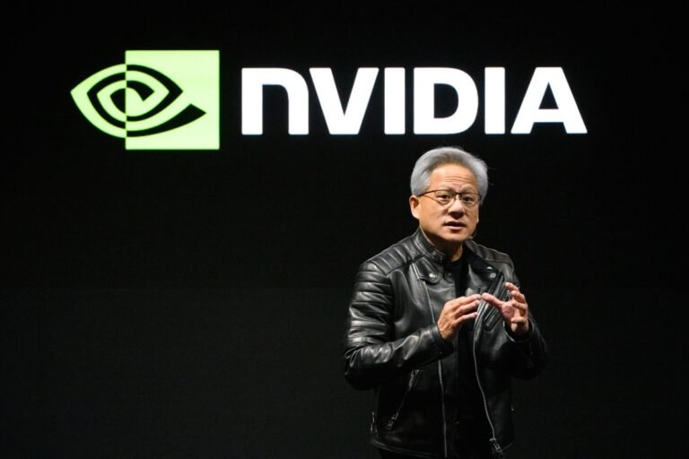 Person in a black leather jacket speaking on stage, Nvidia logo displayed on screen behind them.