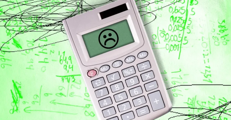 Calculator with a sad face on screen over green paper filled with handwritten mathematical equations and scribbles.