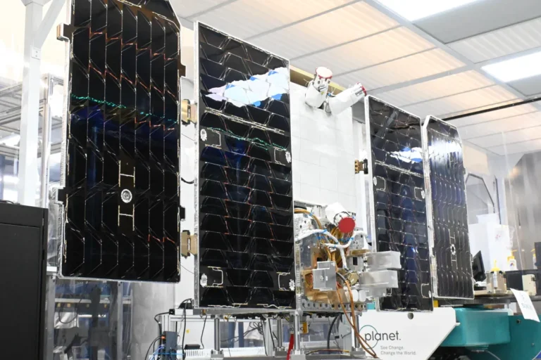 Satellite with solar panels in a laboratory setting, labeled "Planet. See Change. Change the World.