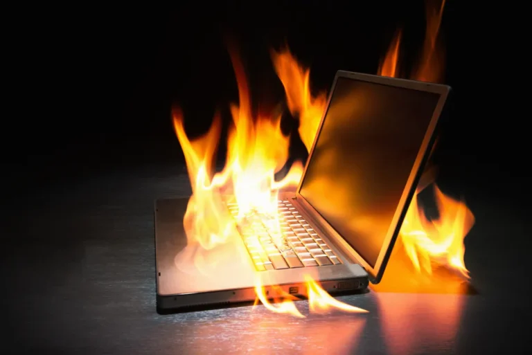 Laptop engulfed in flames on a dark background, symbolizing a cybersecurity threat or urgent tech issue.