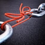 Metal chain link tied with a red rope against a dark background