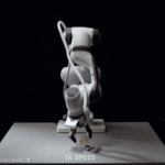 Robotic arm with a gripper holding a small object on a table, dark background, text "1X SPEED" and "EKA" visible