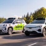 Two white autonomous vehicles with inDrive and pony.ai logos driving on a road with trees in the background.