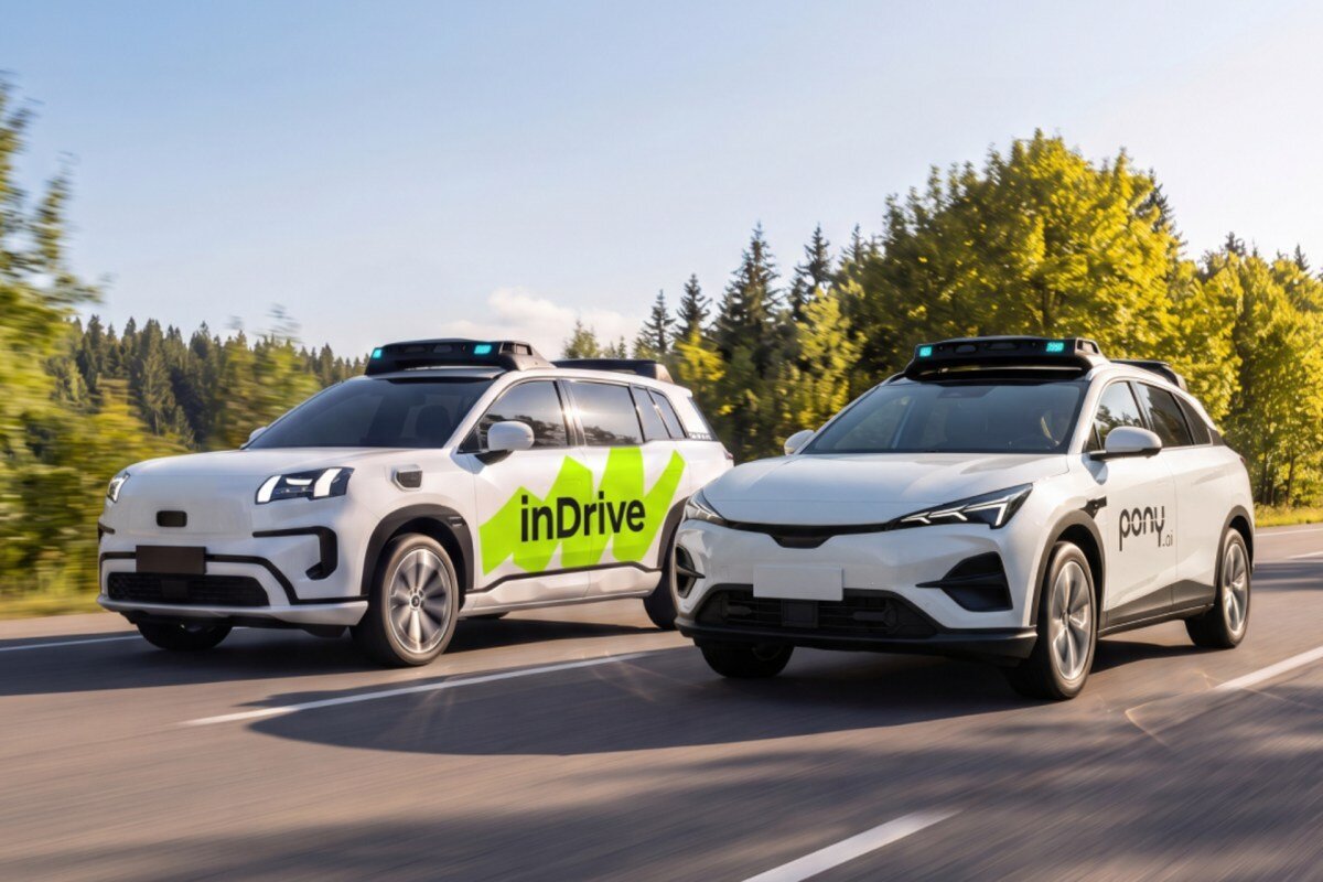 Two white autonomous vehicles with inDrive and pony.ai logos driving on a road with trees in the background.