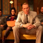 Four people sitting on a yellow couch in a vintage room; one in a suit, others in casual attire, looking intently ahead.