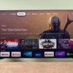 Smart TV interface displaying "The Mandalorian," with app icons for YouTube, Netflix, and more, on a wooden surface.
